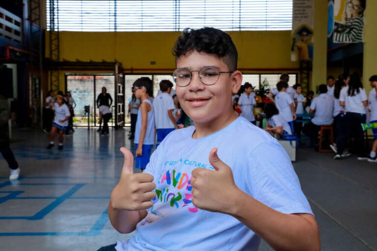 menino que faz aula de robotica no patio da escola fazendo legal com as mãos